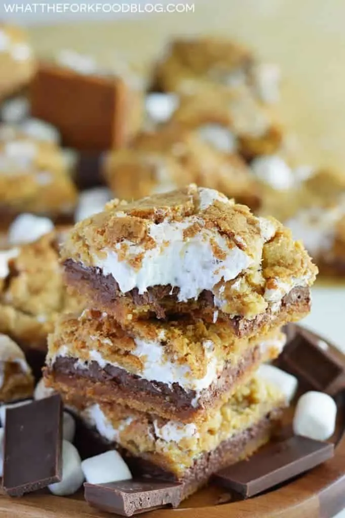 Gluten Free S'mores Bars stacked on a brown wood platter with a bite taken out from What The Fork Food Blog