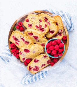 Slices of gluten free raspberry quick bread on a round wood platter garnished with fresh raspberries