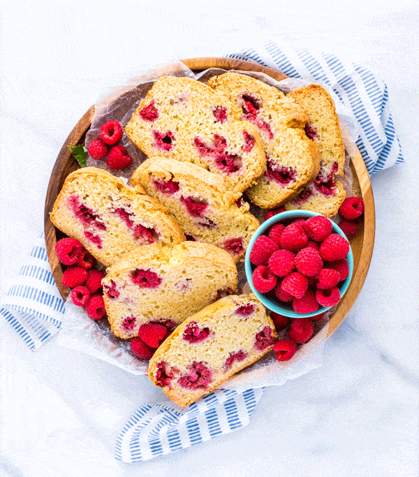 Slices of gluten free raspberry quick bread on a round wood platter garnished with fresh raspberries