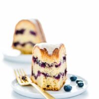 Piece of Gluten Free Blueberry Coffee Cake on a white plate garnished with blueberries and a gold fork.