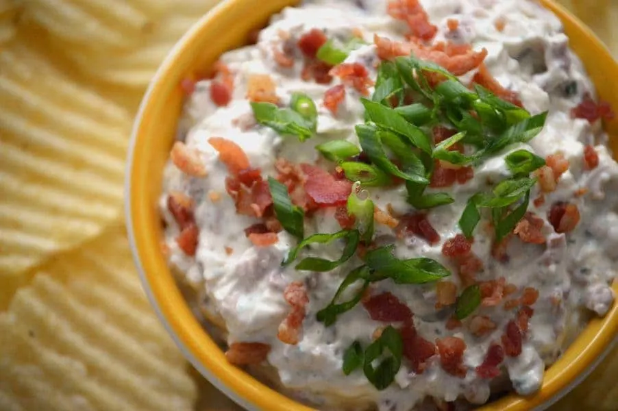 Crack Dip in a bowl, topped with scallions and bacon.