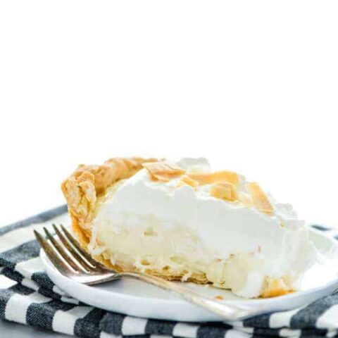 A slice of gluten free coconut cream pie on a white plate with a fork and a black and white striped napkin
