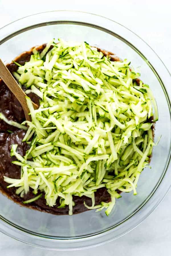 Grated zucchini and batter in a bowl with a wooden spoon to make gluten free double chocolate zucchini bread