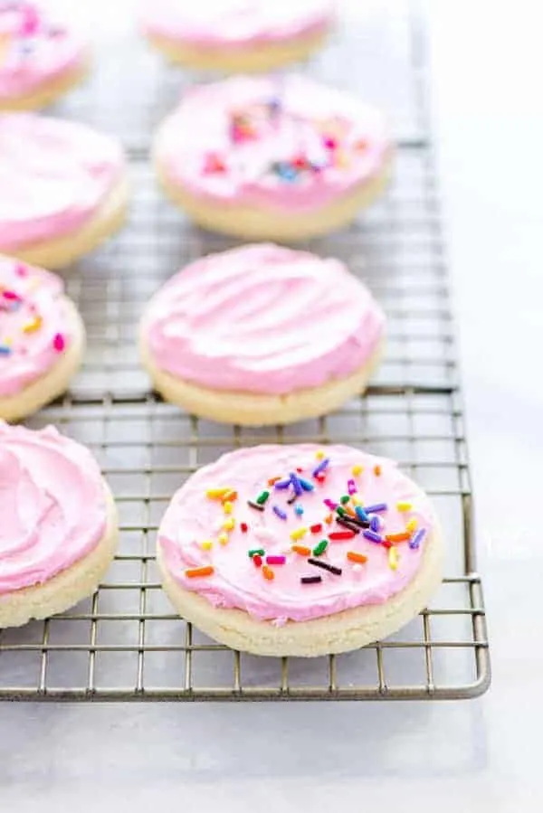 Gluten Free Frosted Sugar Cookies on a wire rack decorated with pink frosting and rainbow sprinkles