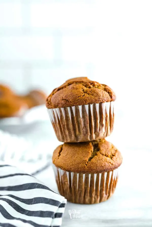 two stacked gluten free pumpkin muffins next to a black and white striped towel