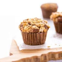 A gluten free banana oat muffin on wax paper on top of a wood cutting board