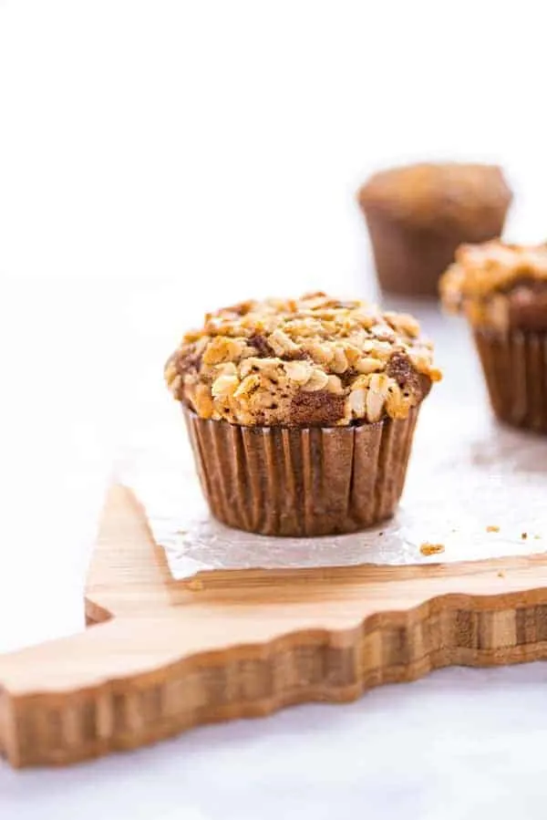 A gluten free banana oat muffin on wax paper on top of a wood cutting board