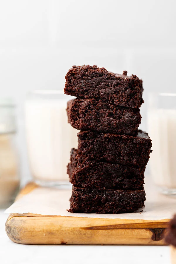 Thick and chewy gluten free brownies stacked on a wood cutting board lined with white parchment paper