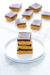 3 gluten free chocolate peanut butter bars stacked on a white plate.