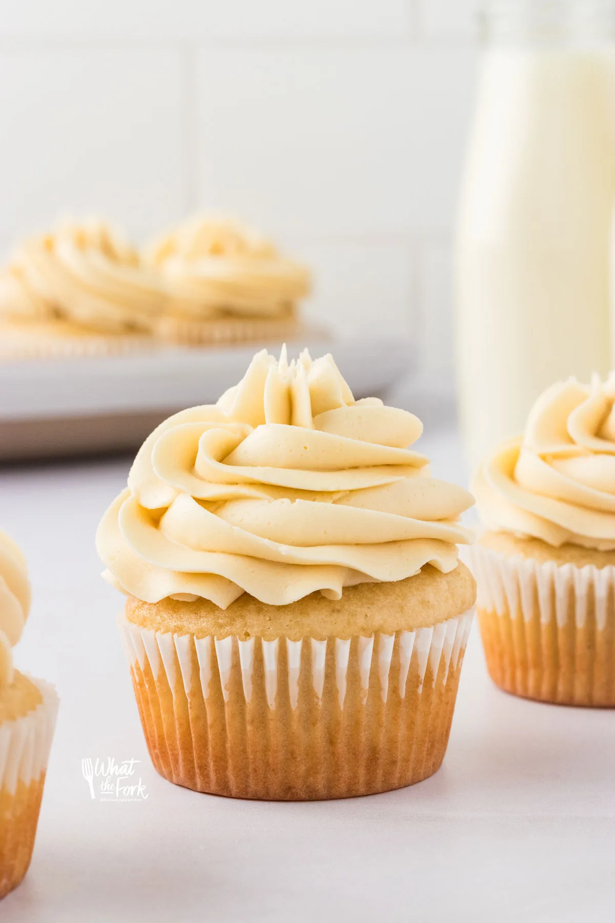 a gluten free vanilla cupcake with a white paper wrapper frosted with vanilla buttercream frosting
