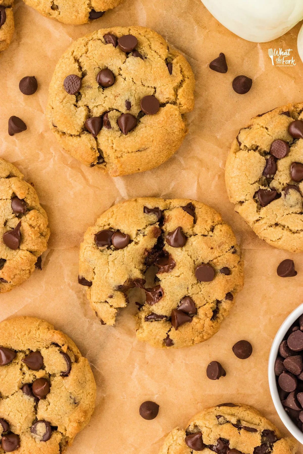 over head shot of gluten free chocolate chip cookies on brown parchment paper with one cookie pulled apart to highlight the gooey chocolate