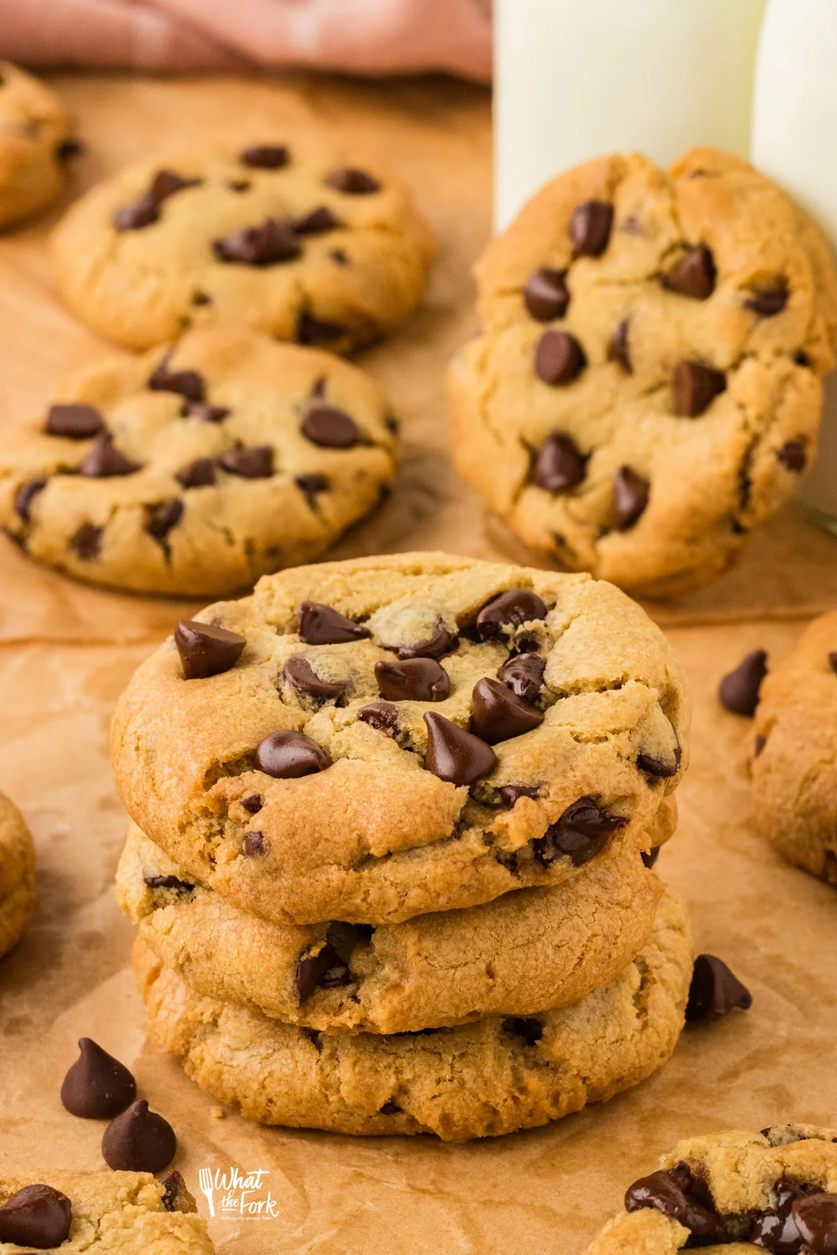 a stack of 3 gluten free chocolate chip cookies on a brown parchment paper with more cookies in the background