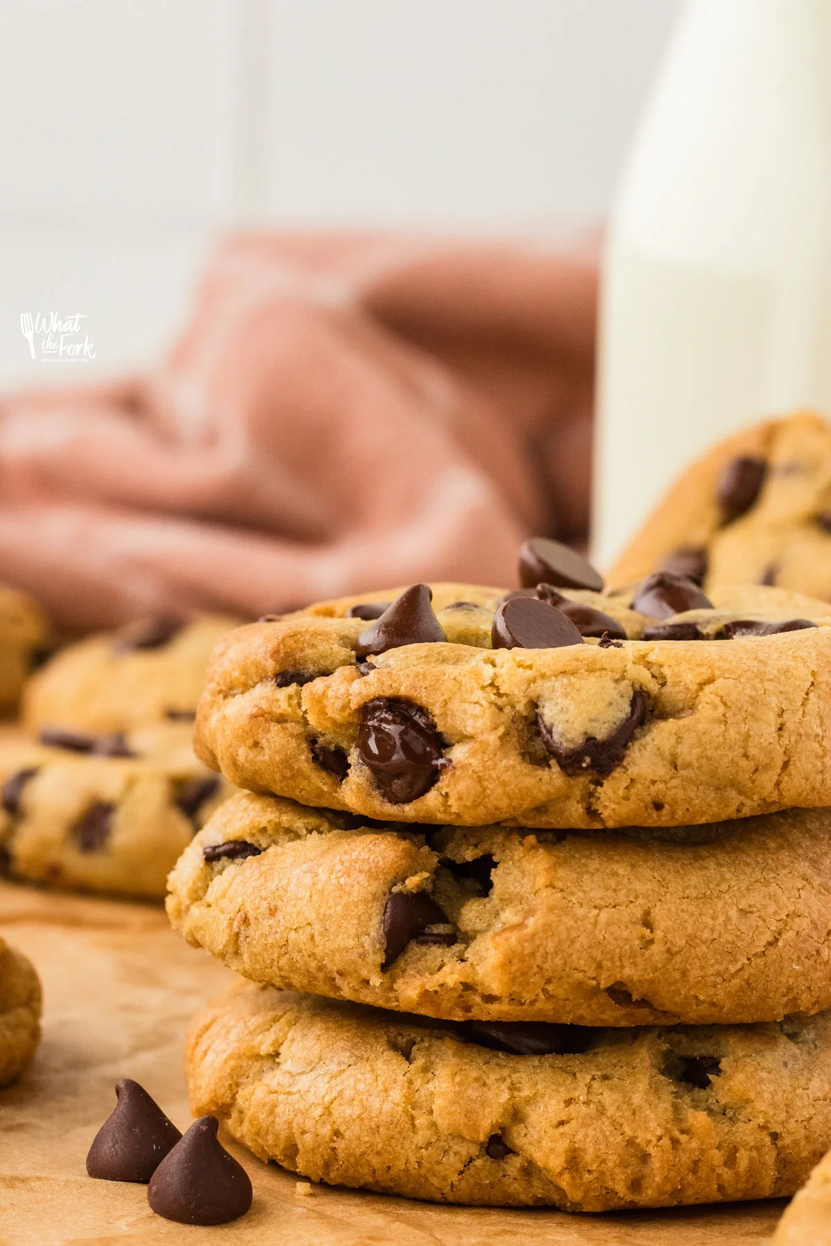 a stack of 3 gluten free chocolate chip cookies with a bottle of milk in the background