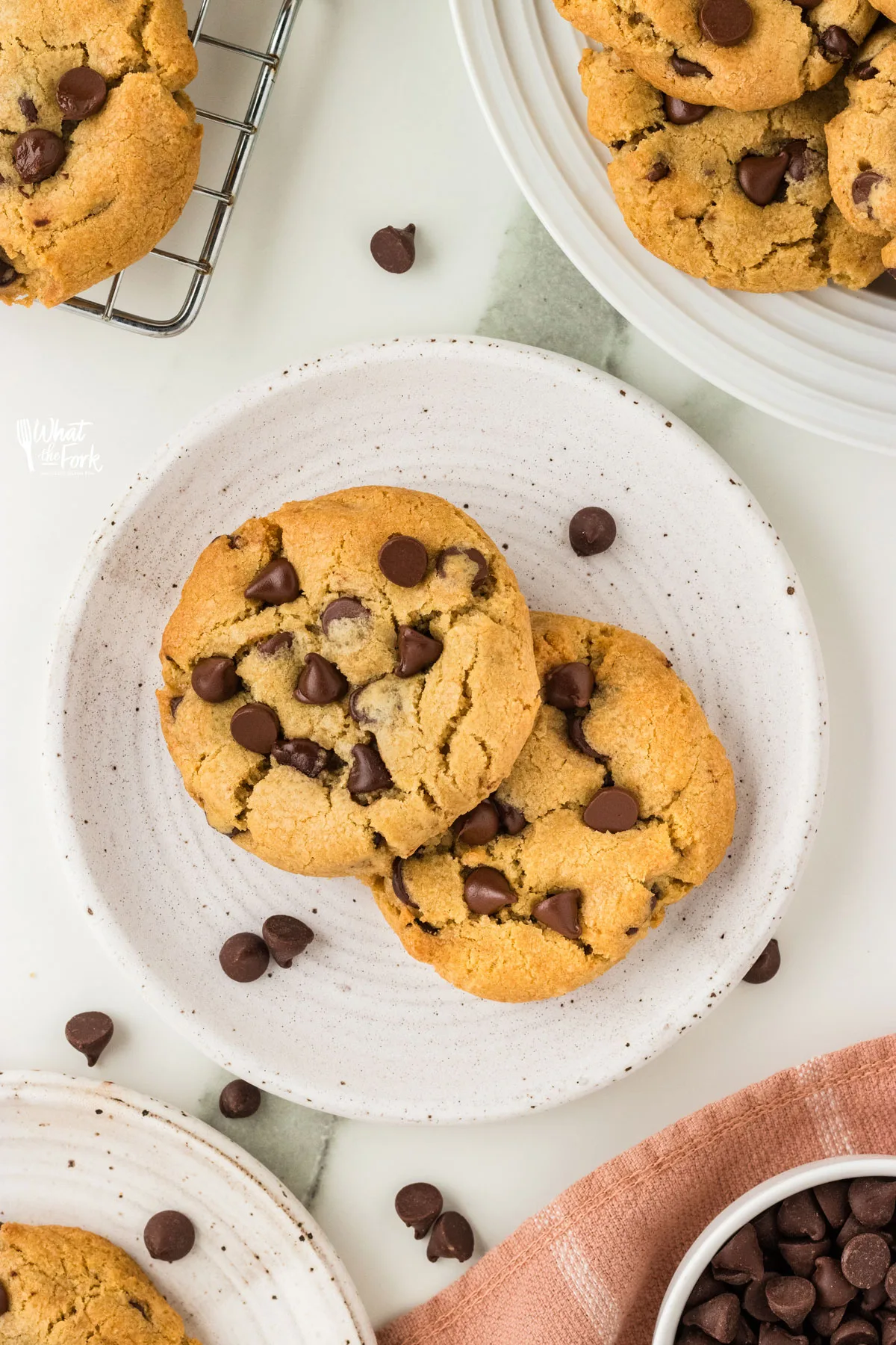 two Thick and Chewy Gluten Free Chocolate Chip Cookies on a small round white plate with chocolate chips scattered around