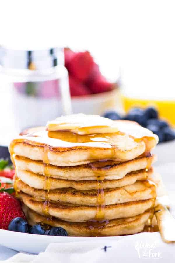 A stack of fluffy and thick gluten free pancakes, drizzled with syrup and topped with butter.