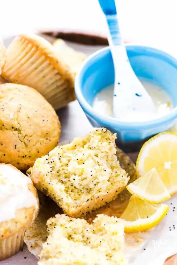 Half of a gluten free lemon poppy seed muffin on a wood platter of muffins.