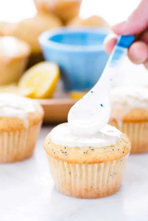 Using a spoon to put lemon glaze on a gluten free lemon poppy seed muffin