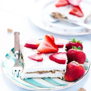 A piece of Gluten Free Strawberry Icebox Cake on a green and white striped plate with a fork. Plate is garnished with whole strawberries.