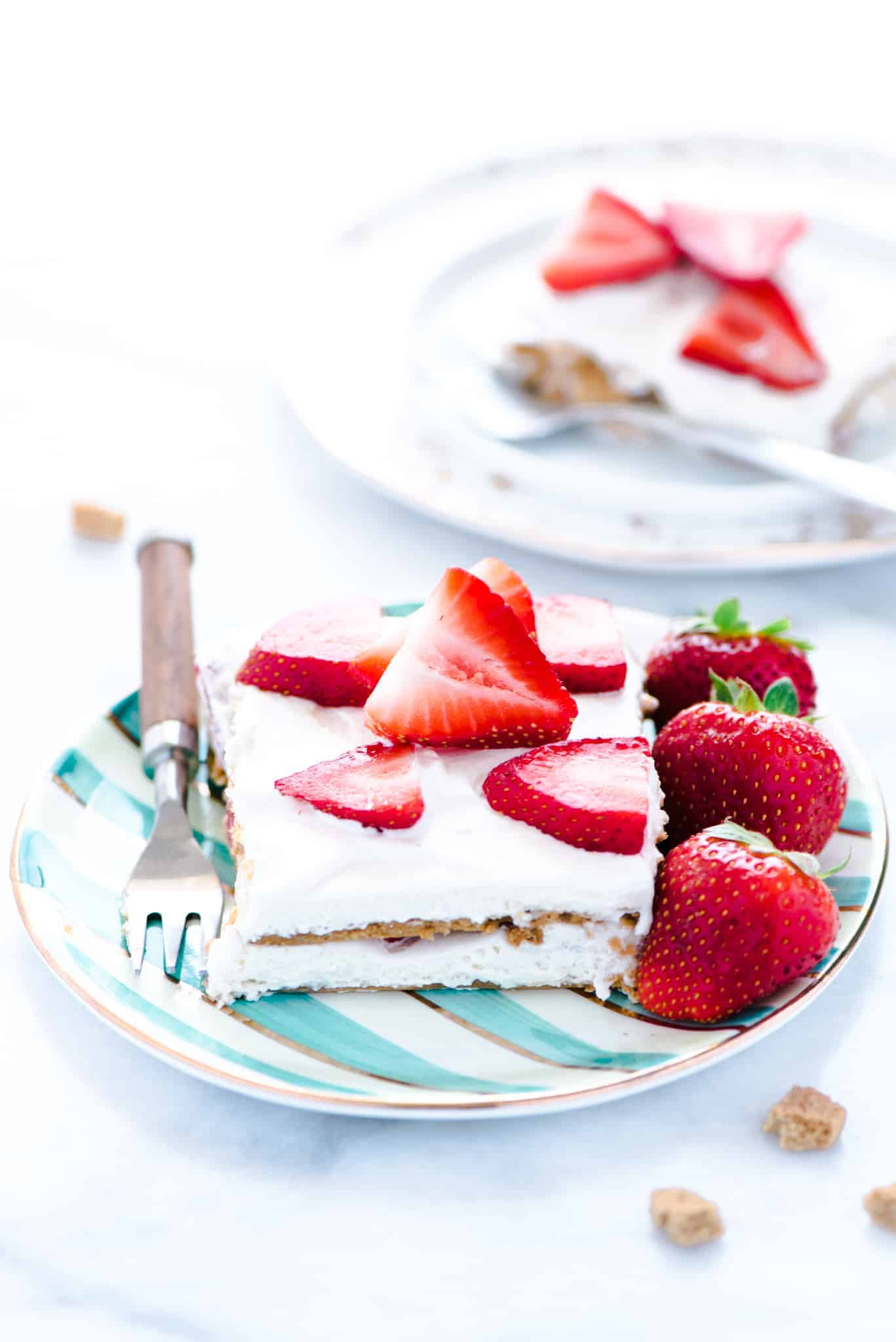 A piece of Gluten Free Strawberry Icebox Cake on a green and white striped plate with a fork. Plate is garnished with whole strawberries.