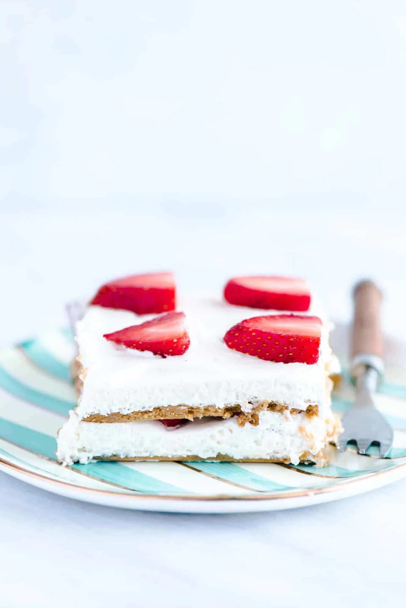 A slice of gluten free strawberry icebox cake on a green and white striped plate