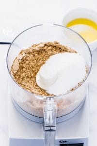Graham cracker crumbs and granulated sugar in a food processor to show how to make a gluten free graham cracker crust