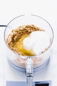 Crushed graham cracker crumbs, melted butter, and granulated sugar in a food processor to show how to make a graham cracker crust