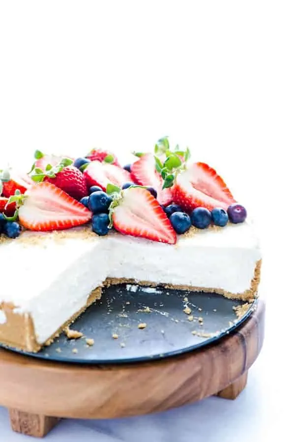 View of sliced no bake cheesecake with fresh berries on a wooden cake stand