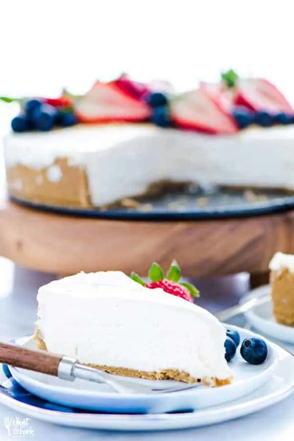 Slice of no bake cheesecake on a plate with a fresh strawberry and blueberries.