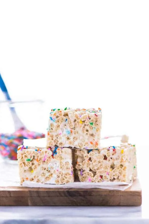 Three Gluten Free Rice Krispies Treats stacked on a brown wood cutting board