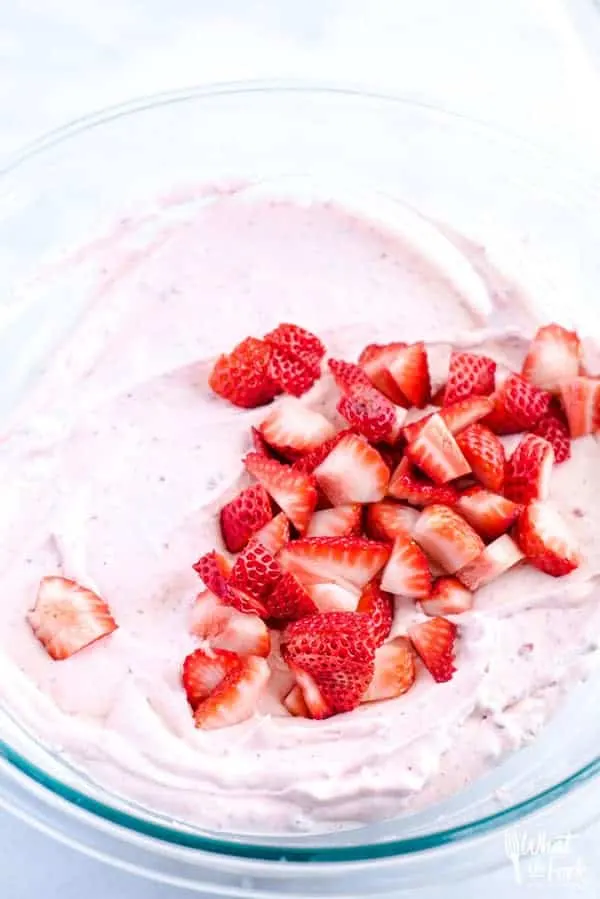 Chopped fresh strawberries in a bowl on top of strawberry whipped cream