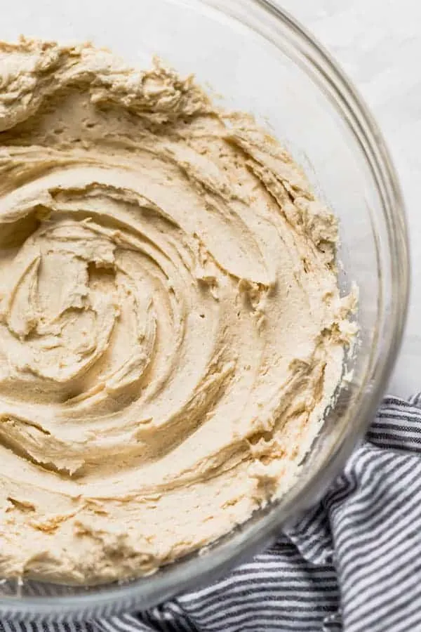 Peanut Butter Frosting in a clear bowl on the table with a blue and white striped towel