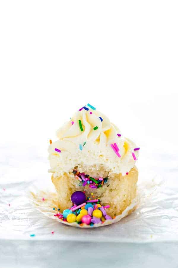 Bite taken out of a Gluten Free Vanilla Piñata Cupcakes with vanilla buttercream frosting and sprinkles.