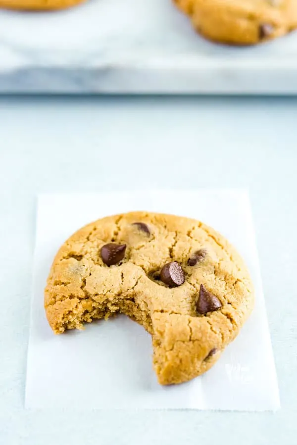 Gluten Free Peanut Butter Chocolate Chip Cookie on a piece of white parchment paper with a bite taken out.