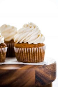 Gluten Free Pumpkin Cupcakes with Cinnamon Cream Cheese Frosting on a wood cake stand