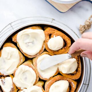 Spreading cream cheese icing on a pan of gluten free cinnamon rolls