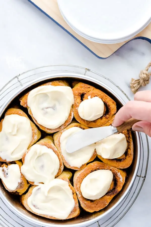 Spreading cream cheese icing on a pan of gluten free cinnamon rolls