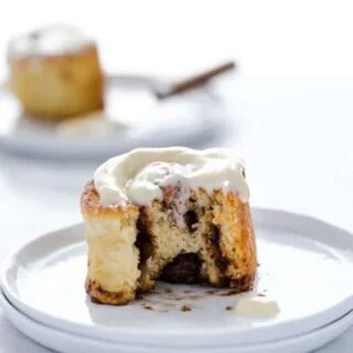 A gluten free cinnamon roll on a white plate with a bite taken out