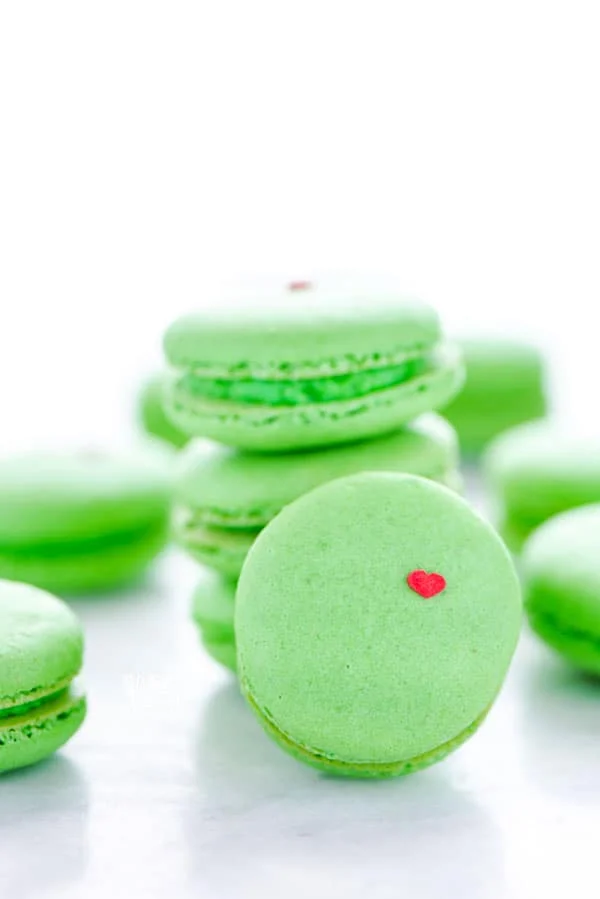 A stack of green Grinch Heart Macarons on a white marble surface