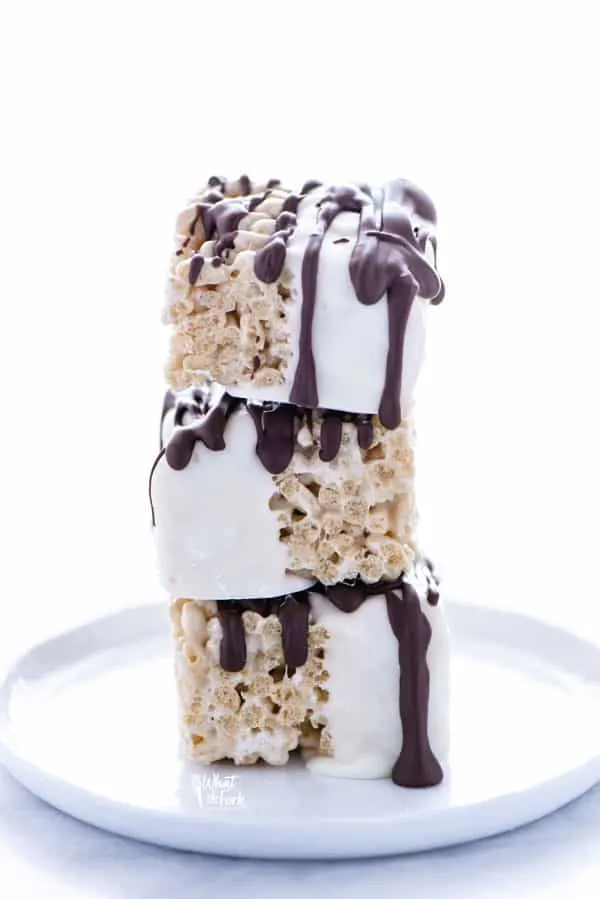 A stack of three chocolate dipped Rice Krispie Treats on a white plate.