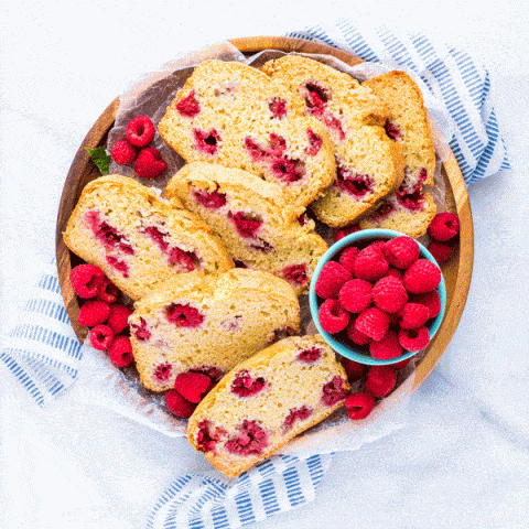 slices of gluten free raspberry quick bread on a wood platter with fresh raspberries