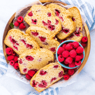 slices of gluten free raspberry quick bread on a wood platter with fresh raspberries