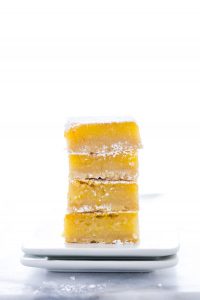 A stack of four gluten free Meyer Lemon Bars on a square white plate