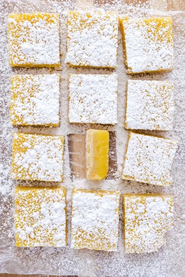 Sliced gluten free Meyer Lemon Bars on a cutting board dusted with powdered sugar