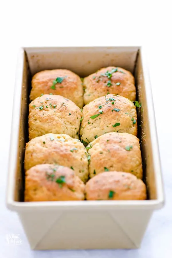 8 gluten free rolls in a gold loaf pan that are brushed with melted butter and topped with fresh parsley and garlic salt