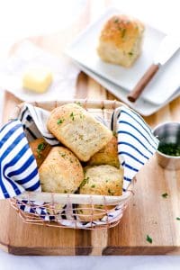 Gluten Free Rolls in a wire basket with a blue and white striped napkin placed on a wood cutting board