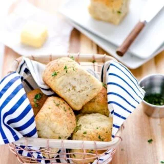 Gluten Free Rolls in a wire basket with a blue and white striped napkin placed on a wood cutting board