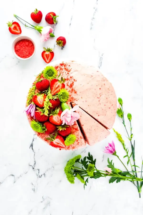 Overhead shot of a gluten free strawberry cake garnished with fresh strawberries and flowers