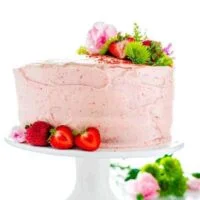 Homemade Gluten Free Strawberry Cake on a white cake stand garnished with fresh strawberries and flowers