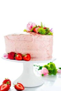 Homemade Gluten Free Strawberry Cake on a white cake stand garnished with fresh strawberries and flowers
