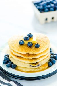 gluten free blueberry pancakes stacked on a plate and garnished with a pat of butter and fresh blueberries
